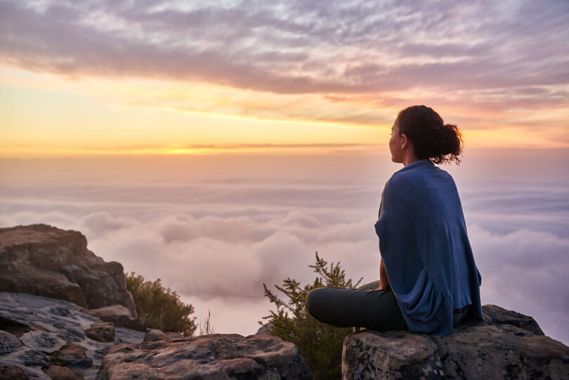 Frau meditiert auf Berg über den Wolken
