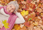 Eine Frau liegt lachend im Herbstlaub auf dem Boden