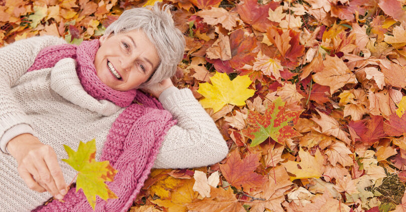 Eine Frau liegt lachend im Herbstlaub auf dem Boden